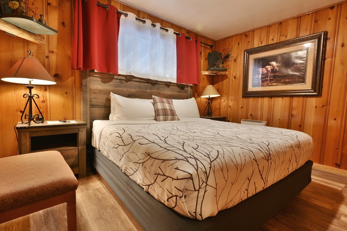 A cozy room with a king-sized bed, wooden paneling, and rustic decor.